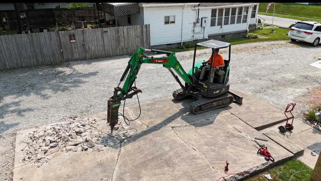 Mini excavator with a hydraulic breaker taking apart an old concrete slab